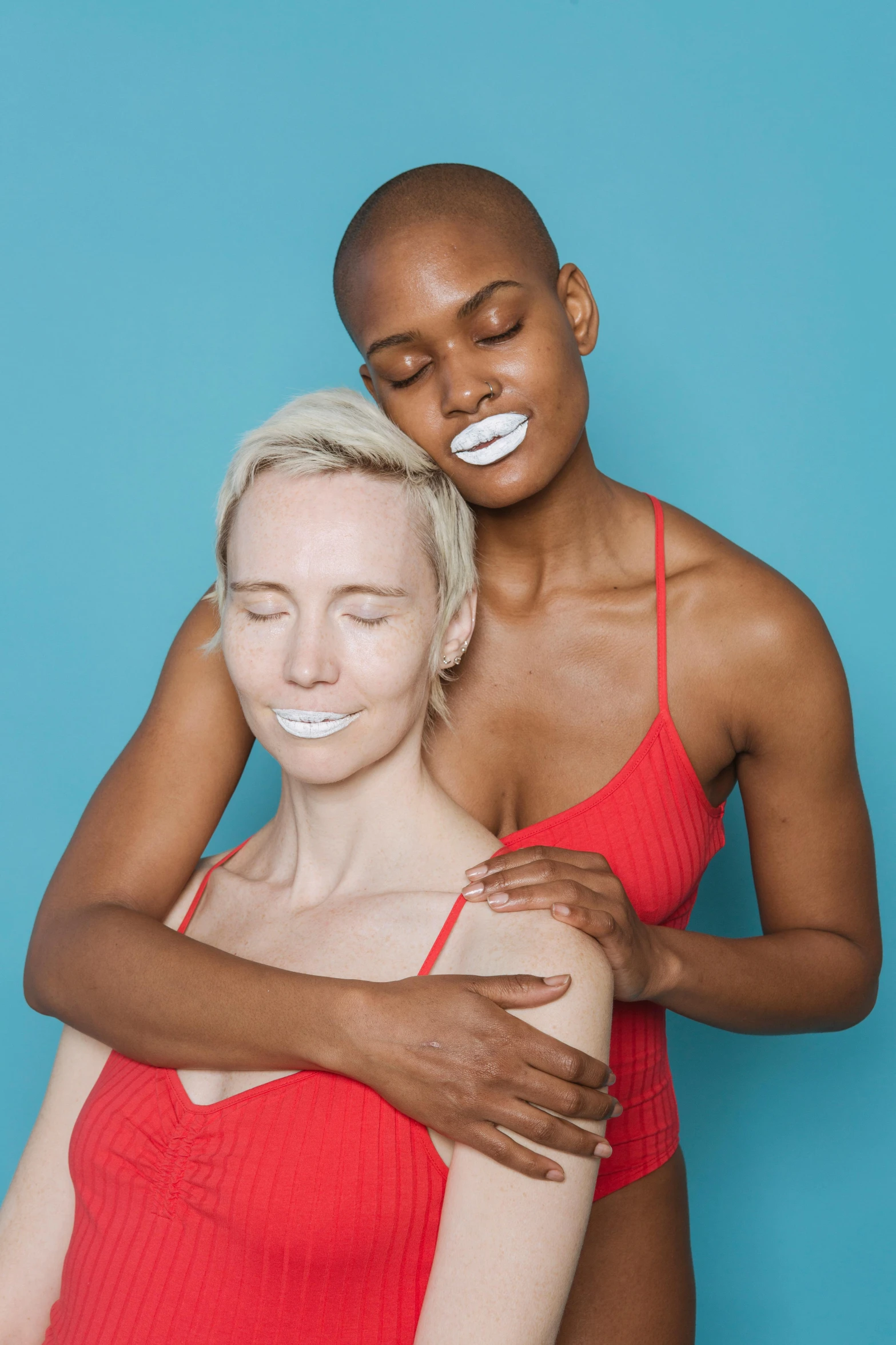 a woman in a red bathing suit hugging a woman in a red bathing suit, inspired by Vanessa Beecroft, white powder makeup, portrait of ororo munroe, her iridescent membranes, porcelain holly herndon statue