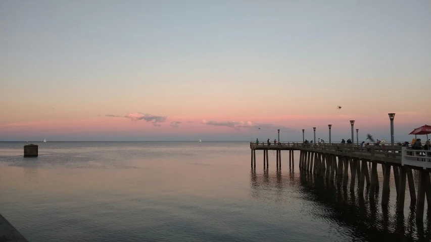 a pier that is next to a body of water, a picture, sky setting, overlooking the ocean, image from afar, the sky is pink