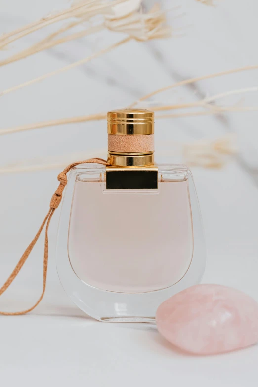 a bottle of perfume next to a pink stone, lasso, zoomed in, displayed, feminine features