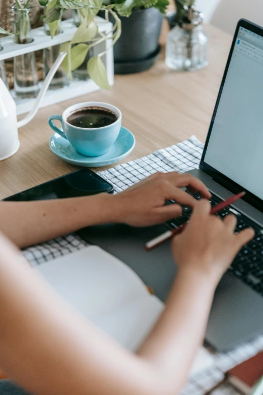 a woman sitting at a table using a laptop computer, trending on pexels, table in front with a cup, thumbnail, multiple stories, from waist up