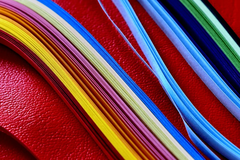 a bunch of different colored ribbons on a red surface, a picture, by Jan Rustem, pexels, color field, paper quilling, closeup portrait, coated pleats, threads