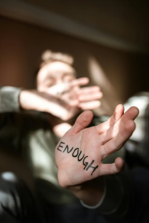 a man holding out his hand with the word enough written on it, trending on pexels, portrait of depressed teen, with violence, blurred, sitting down