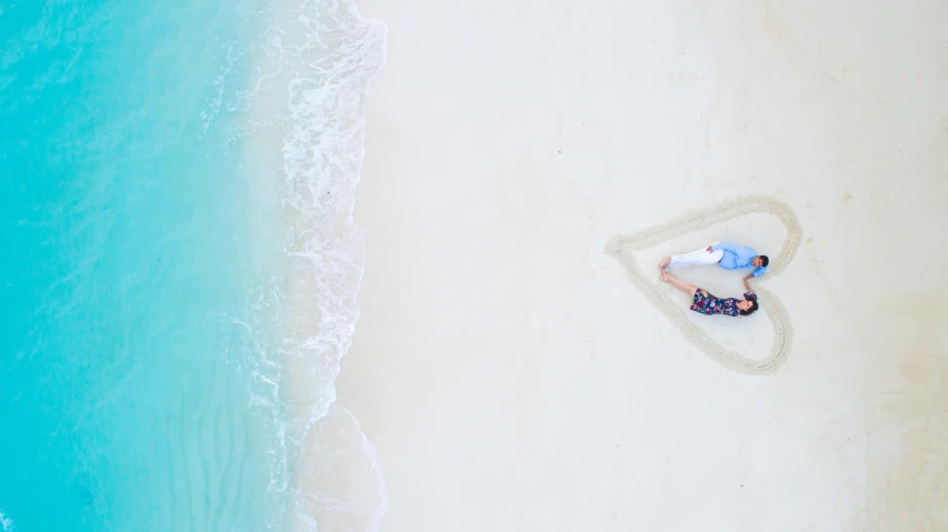 a man laying on top of a sandy beach next to the ocean, pexels contest winner, minimalism, romantic couple, helicopter view, bahamas, pregnancy