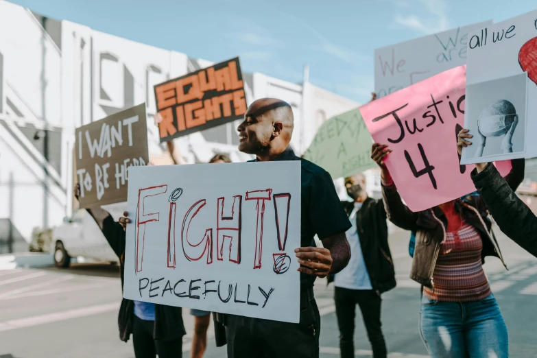 a group of people holding signs in the street, by Julia Pishtar, trending on pexels, black arts movement, background image, fight, peacefull, 3 4 5 3 1