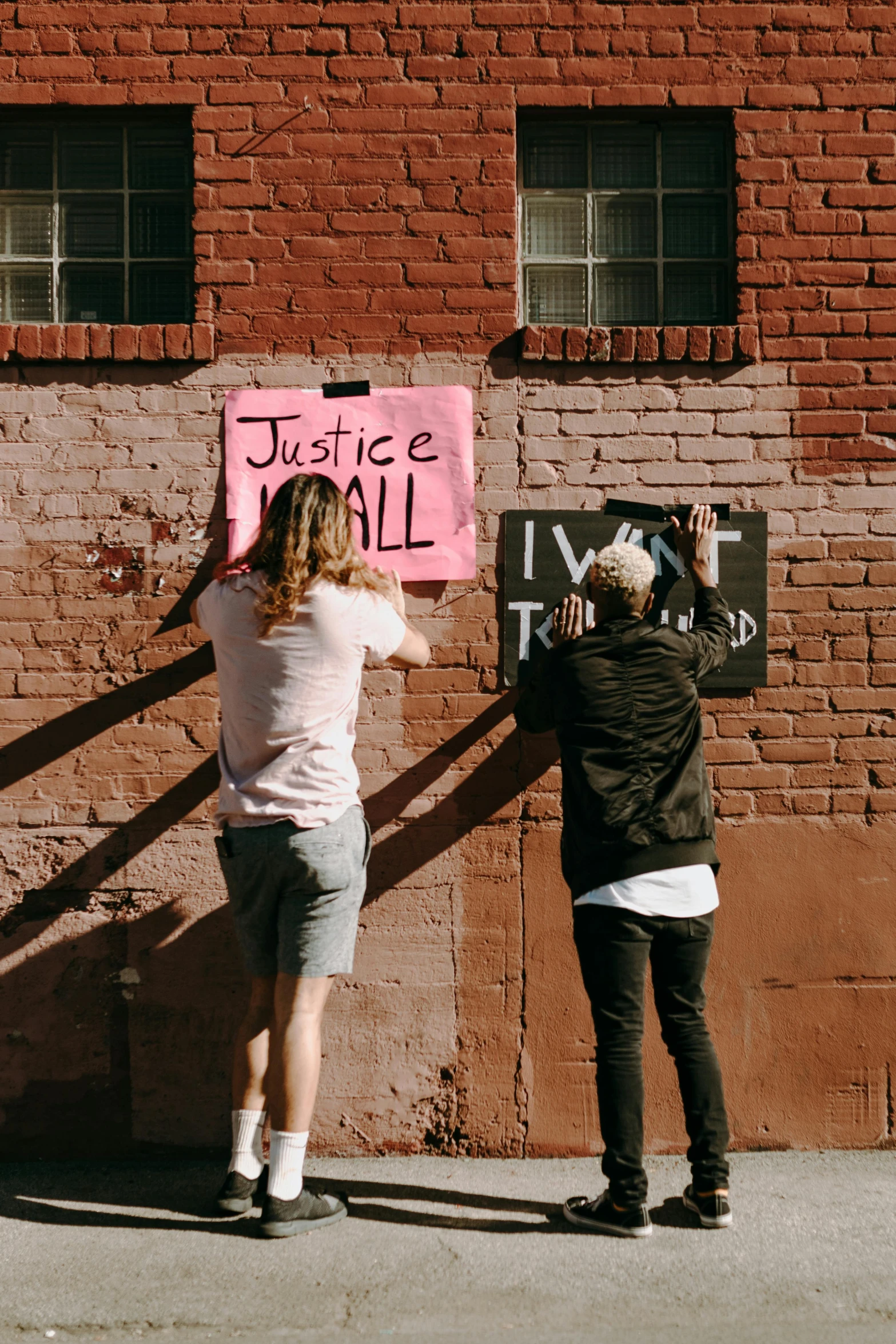 two people hanging a sign on the side of a building, trending on unsplash, graffiti, justice, trans rights, instagram picture, brick walls