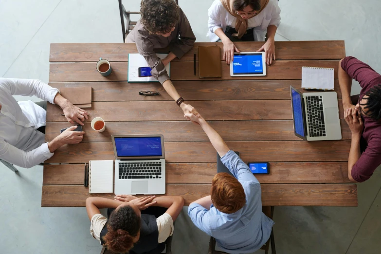 a group of people sitting around a wooden table, a digital rendering, trending on pexels, renaissance, reaching out to each other, professional branding, aerial shot, embracing