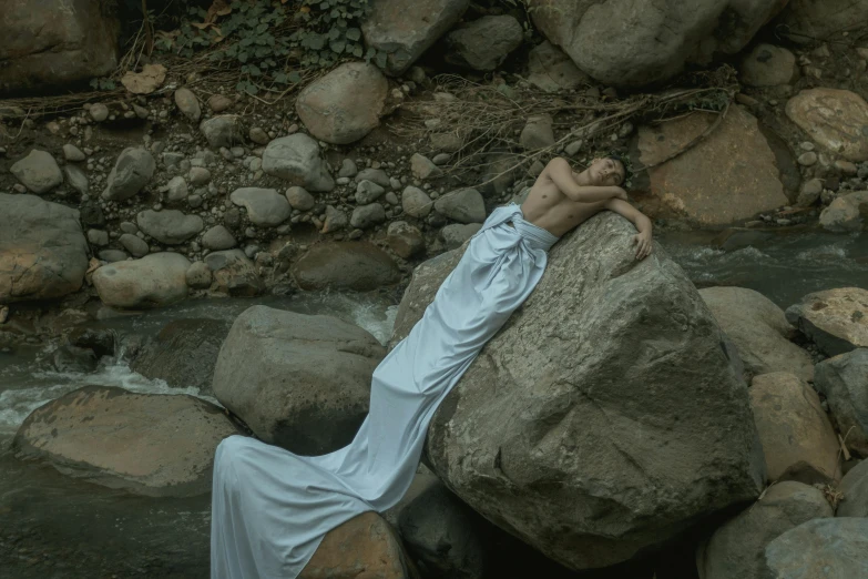 a woman laying on a rock in a river, a statue, inspired by Elsa Bleda, surrealism, standing on rocky ground, grey, ad image, portait image