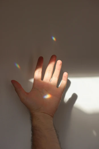 a person holding their hand up against a wall, inspired by Gabriel Dawe, pexels, light and space, light refraction, morning light showing injuries, light scatter, soft shadow