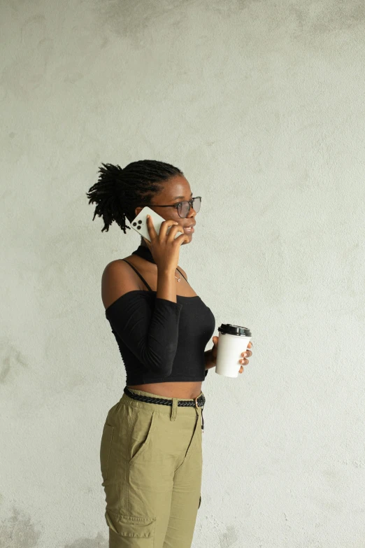 a woman talking on a cell phone while holding a cup of coffee, by Lily Delissa Joseph, minimalism, wearing a crop top, black black black woman, college, holding arms on holsters