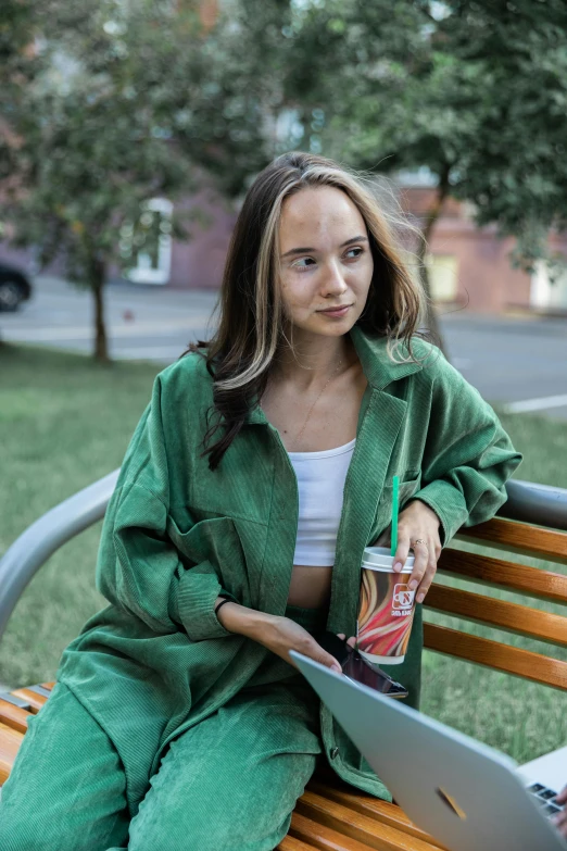 a woman sitting on a bench with a laptop, a portrait, pexels contest winner, realism, green corduroy pants, in russia, holding a drink, long shirt