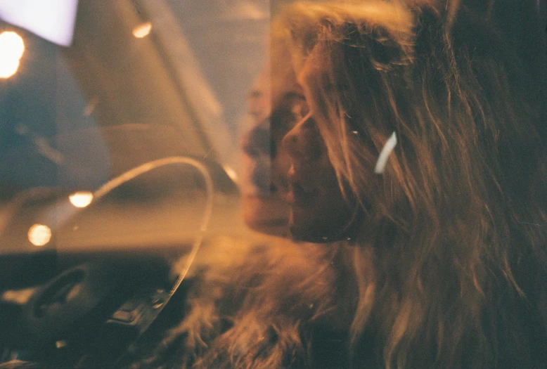 a woman sitting in a car talking on a cell phone, a picture, inspired by Elsa Bleda, trending on pexels, messy blonde hair, 35mm double-exposure photo, warm glow, looking in the mirror