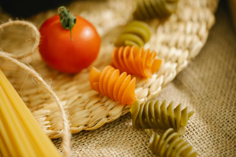 a bunch of pasta and a tomato on a table, by Carey Morris, trending on pexels, wicker art, green and yellow, larvae, 6 pack