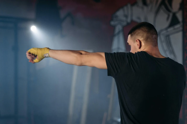a man in a black shirt holding a yellow glove, pexels contest winner, happening, choreographed fight scene, background image, big arms, berghain