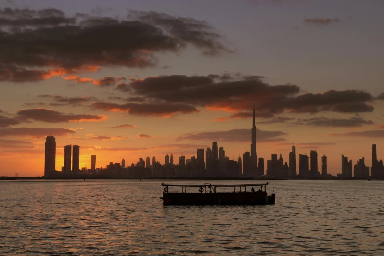 a boat in a body of water with a city in the background, by Liza Donnelly, pexels contest winner, hurufiyya, humid evening, empire silhouette, dubai, conde nast traveler photo