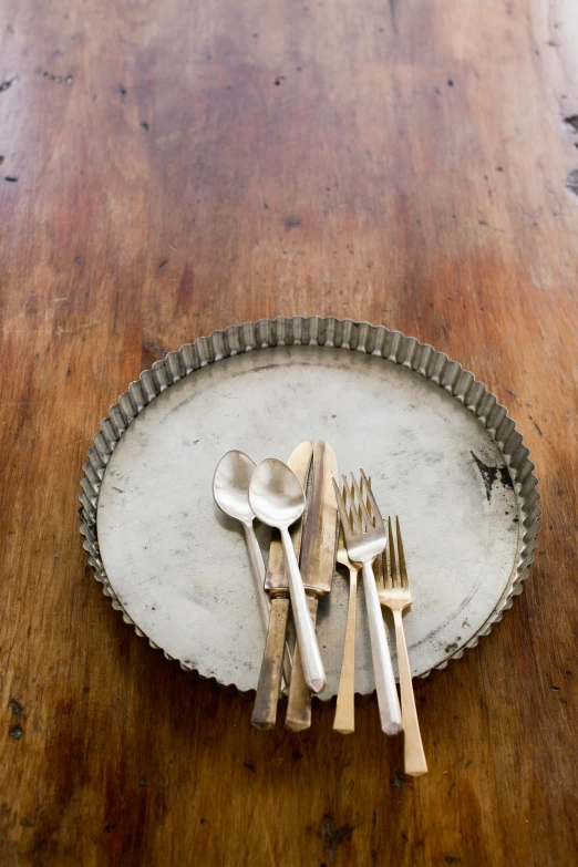 a wooden table topped with silverware on top of a wooden table, folk art, culinary art photography, aluminum, dish, rust