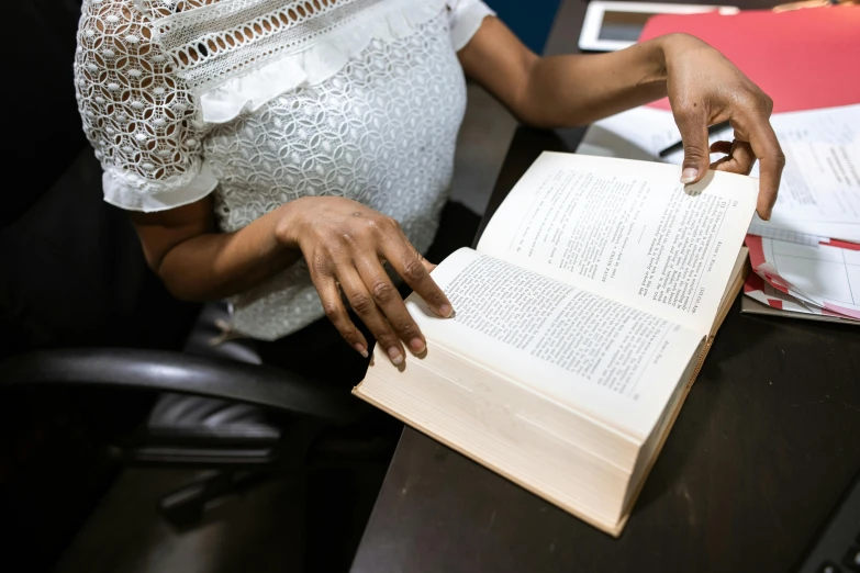 a woman sitting at a desk reading a book, by Carey Morris, pexels contest winner, renaissance, holding it out to the camera, augusta savage, dynamic closeup, people at work