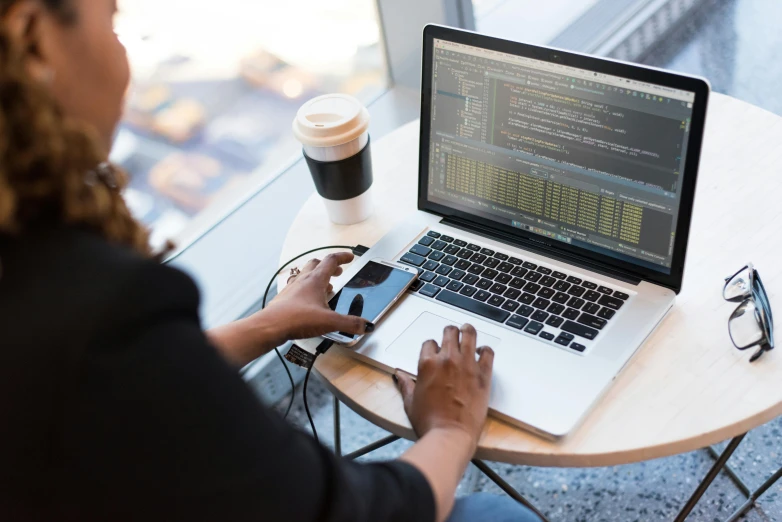 a woman sitting at a table with a laptop and cell phone, unsplash, coding, sitting on a mocha-colored table, engineer, built on a small