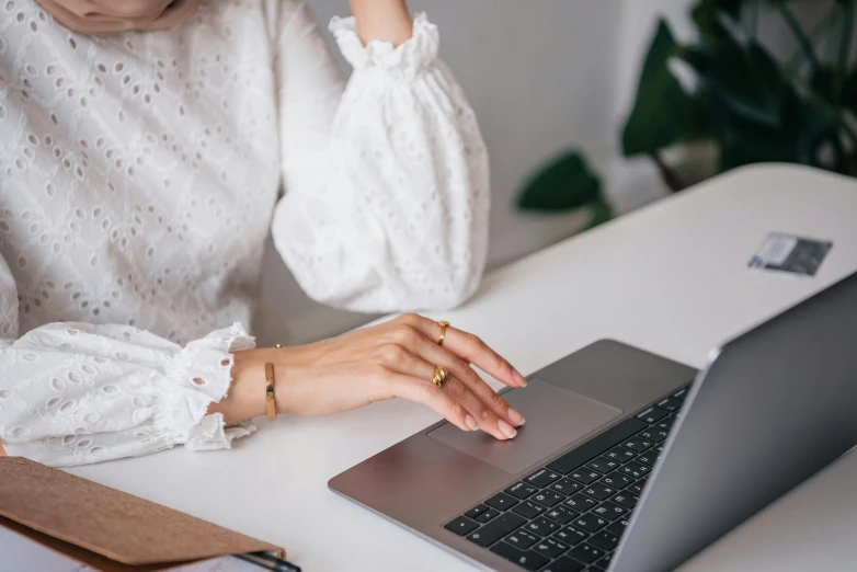 a woman sitting at a desk using a laptop computer, trending on pexels, cream colored blouse, point finger with ring on it, delicate patterned, white