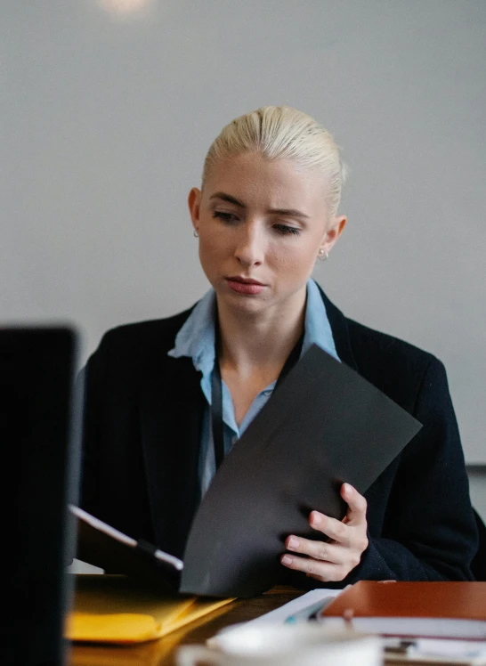 a woman sitting at a desk in front of a laptop, bleached blonde short hair, holding a clipboard, security agent, profile image