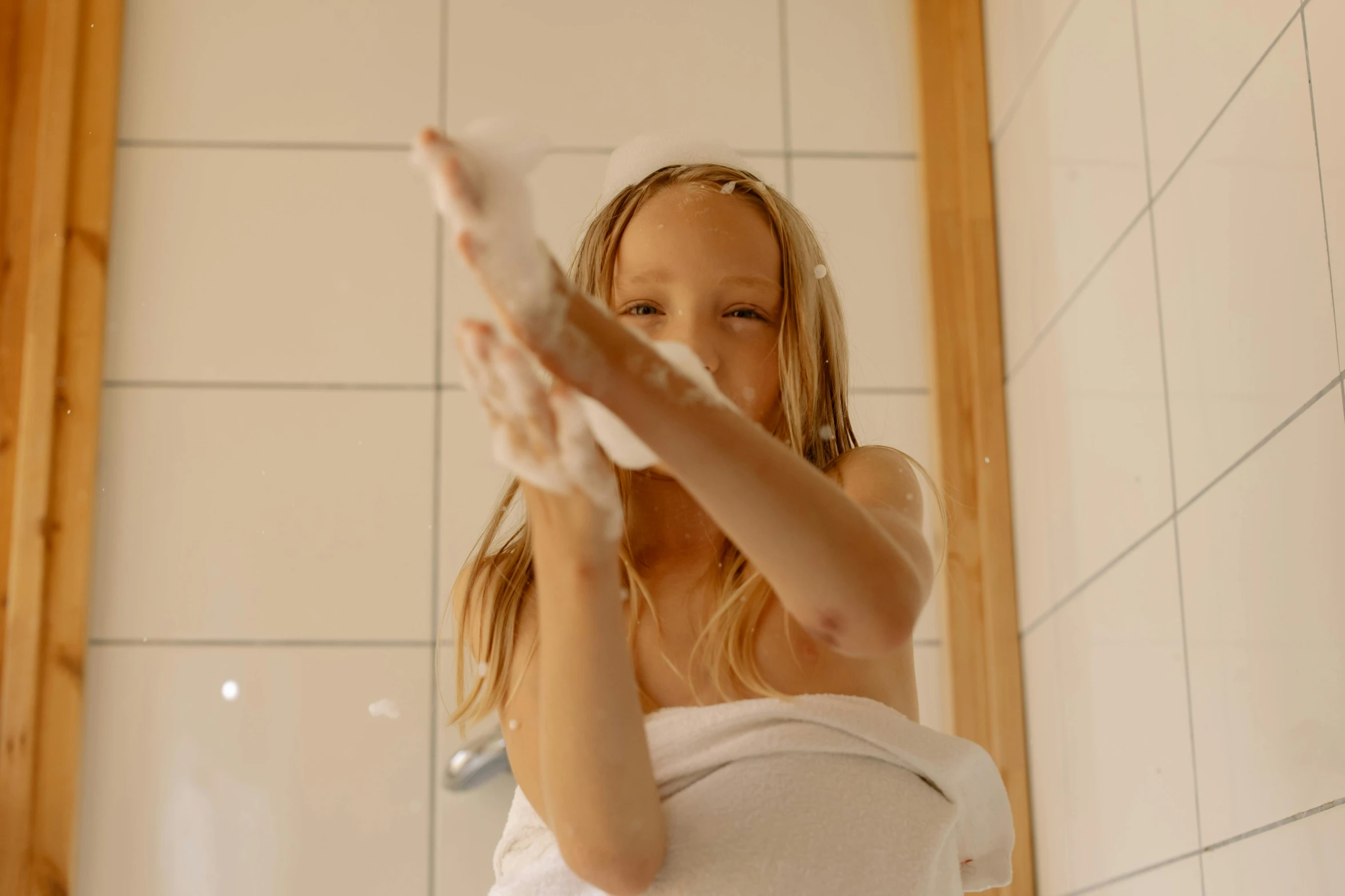 a woman standing in a bathroom with a towel on her head, by Emma Andijewska, pexels contest winner, happy kid, raising an arm, soap, a girl with blonde hair