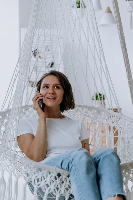 a woman sitting in a hammock talking on a cell phone, pexels contest winner, in a white boho style studio, wearing casual clothing, large)}], realistic »