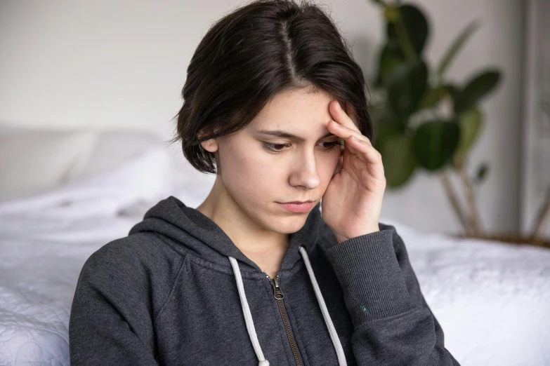 a woman sitting on a bed with her head in her hands, a picture, trending on pexels, hurufiyya, male teenager, spasms, grey, tall forehead