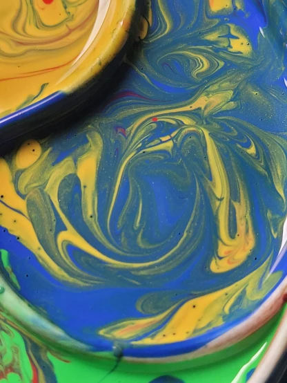 a close up of a plate with paint on it, inspired by Umberto Boccioni, trending on unsplash, yellow and blue, swirling paint colors, r / paintedminis, marbling
