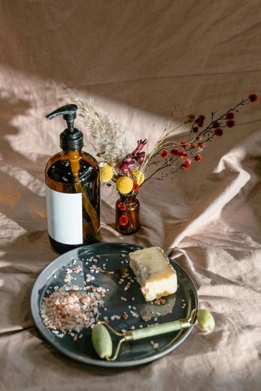 a plate topped with a piece of cake next to a bottle of liquid, a still life, unsplash, baroque, soap, dried flowers, olive oil, black and terracotta