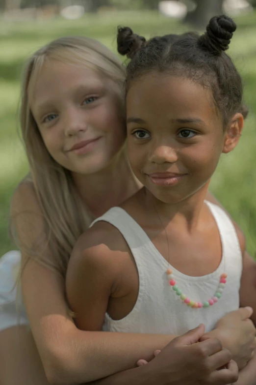 a couple of young girls sitting on top of a lush green field, puka shell necklace, rainbow accents, jr, model