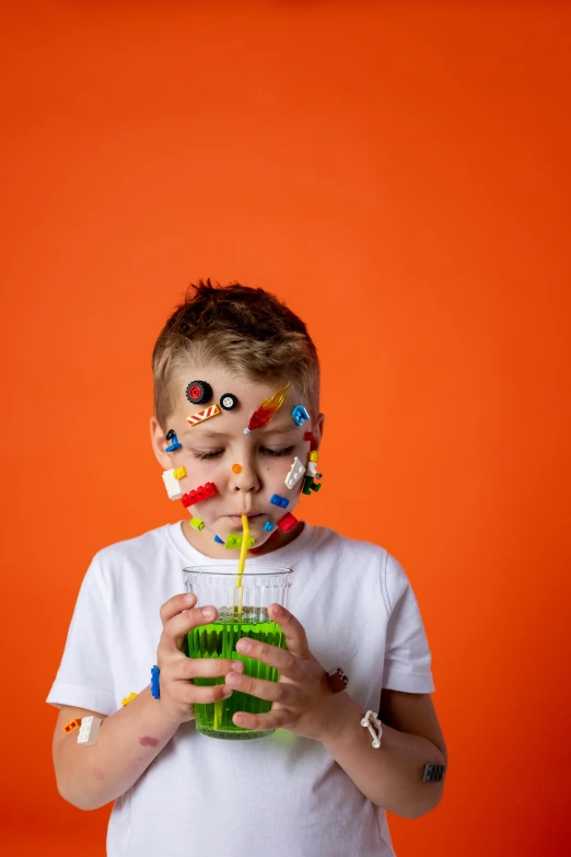 a young boy drinking a drink with sprinkles on his face, an album cover, by Adam Marczyński, pexels, green and orange theme, robots drinking alcohol, made of lollypops, kid a