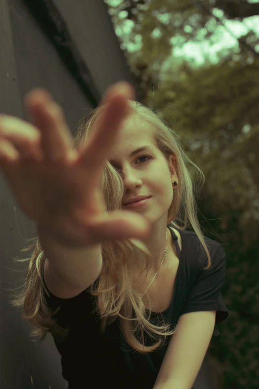 a woman leaning against a wall with her hand in the air, by Anna Boch, unsplash, realism, long blonde hair and large eyes, selfie of a young woman, exactly 5 fingers, grainy quality