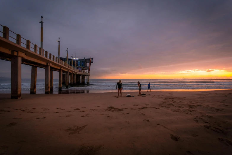 a group of people standing on top of a sandy beach, by Lee Loughridge, unsplash contest winner, near a jetty, predawn, manly, blonde