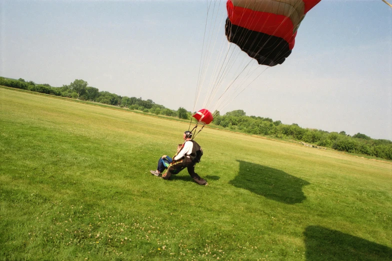 a man that is sitting in the grass with a parachute, flying towards the camera, shot from a distance, far shot, leg shot