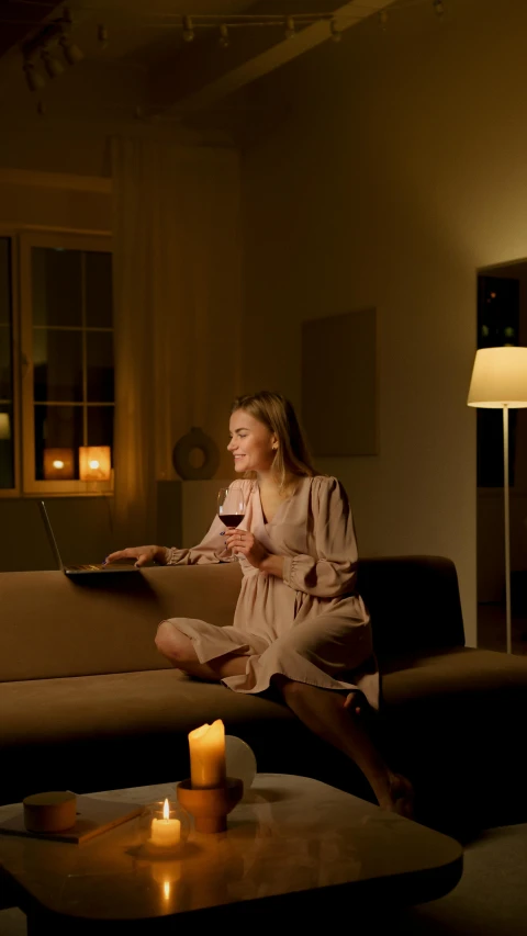 a woman sitting on a couch in a living room, by Jesper Knudsen, pexels contest winner, night light, enjoying a glass of wine, sitting in front of computer, press shot
