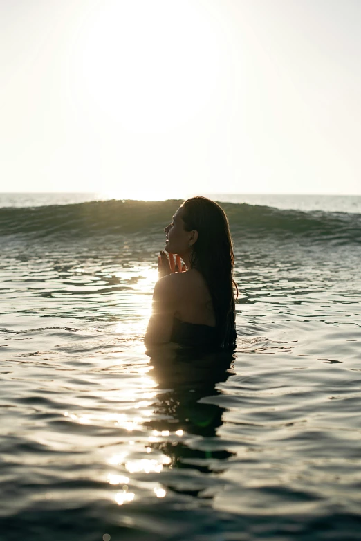 a woman sitting on top of a surfboard in the ocean, flowing backlit hair, half face in the water, trending photo