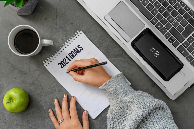 a person writing on a notepad next to a laptop, a photo, by Julia Pishtar, trending on pexels, happening, year 2 0 2 2, style lettering, holding flask in hand, resolution