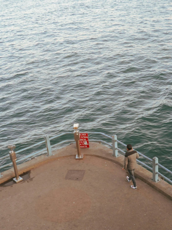 a man standing on top of a pier next to the ocean, a picture, by Elsa Bleda, happening, joel meyerowitz, helipad, low quality footage, tiny person watching