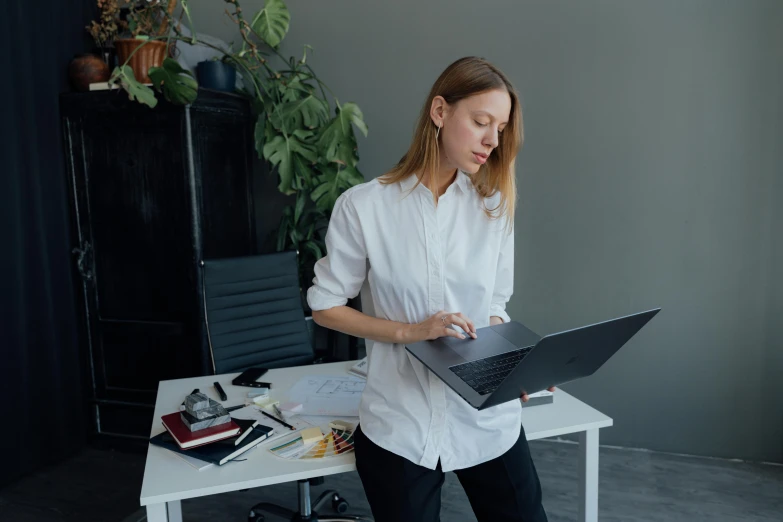 a woman in a white shirt is using a laptop, pexels contest winner, standing on a desk, avatar image, yulia nevskaya, low quality photo