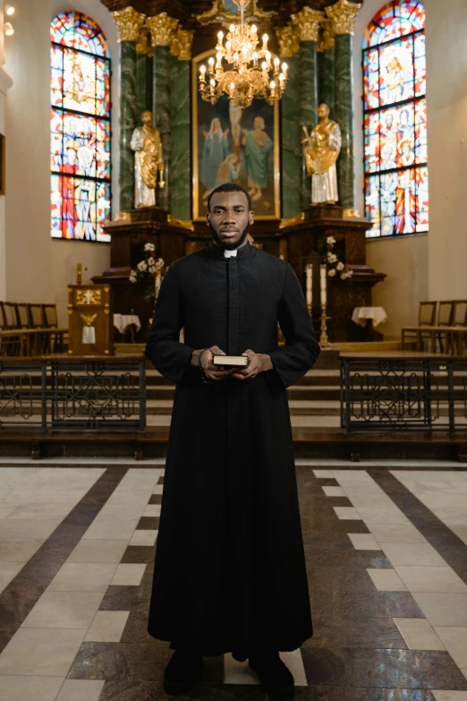 a priest standing in a church holding a book, inspired by Barthélemy d'Eyck, shutterstock, dark skinned, full frontal, black overcoat, photo shoot