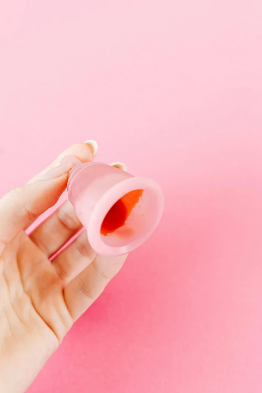 a woman's hand holding a bottle of nail polish on a pink background, by Julia Pishtar, plasticien, shaped like torus ring, awkwardly holding red solo cup, translucent body, viewed from behind