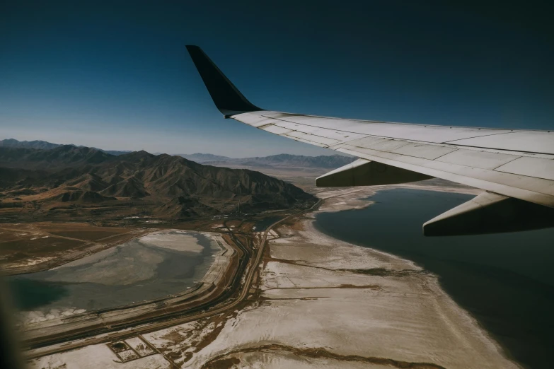 the wing of an airplane flying over a body of water, by Carey Morris, pexels contest winner, modernism, deserts and mountains, runway, plain background, hd footage