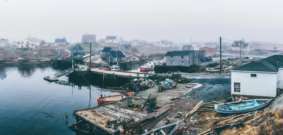 a boat sitting on top of a body of water, a colorized photo, by Carey Morris, pexels contest winner, buildings covered in black tar, small port village, hazy and dreary, wood pier and houses