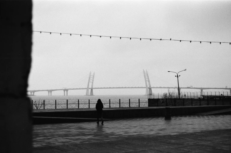 a black and white photo of a person walking in the rain, a black and white photo, postminimalism, connected with hanging bridge!!, zezhou chen, harbor, anna nikonova