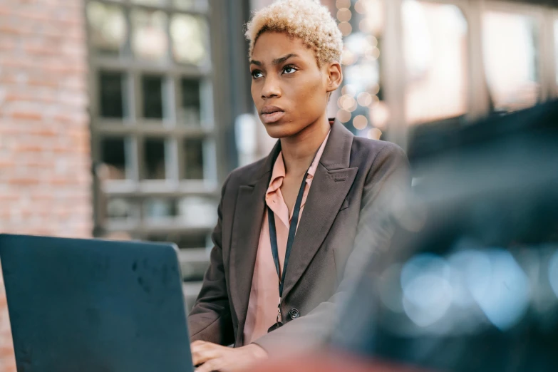 a woman sitting in front of a laptop computer, by Carey Morris, trending on pexels, short blonde afro, serious business, worksafe. instagram photo, wearing jacket and skirt