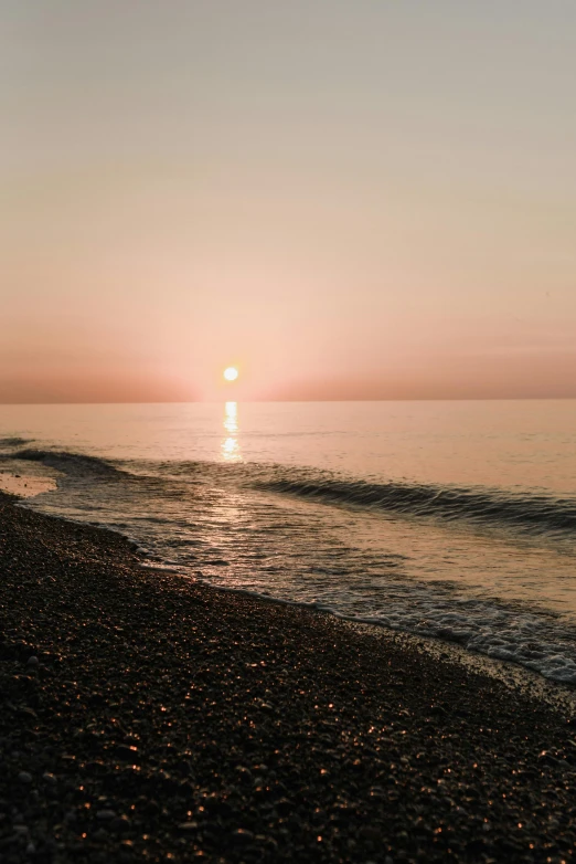 a man standing on top of a beach next to the ocean, unsplash contest winner, romanticism, pink sun, black sea, at sunrise in springtime, calm waves