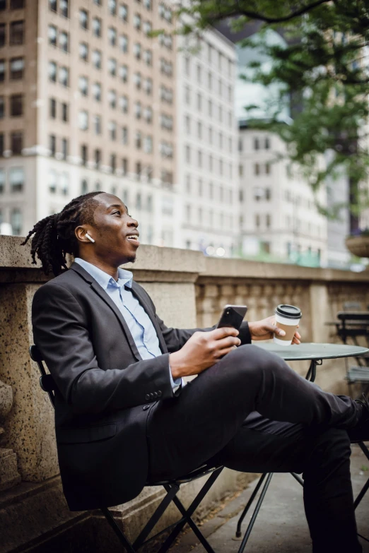 a man sitting at a table with a cup of coffee, in new york city, listening to music, promotional image, sitting on bench