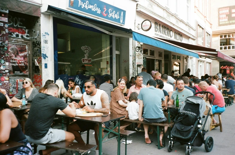 a group of people sitting at tables outside of a restaurant, a photo, by Niko Henrichon, milk bar magazine, worst place to live in europe, with street food stalls, s baraldi