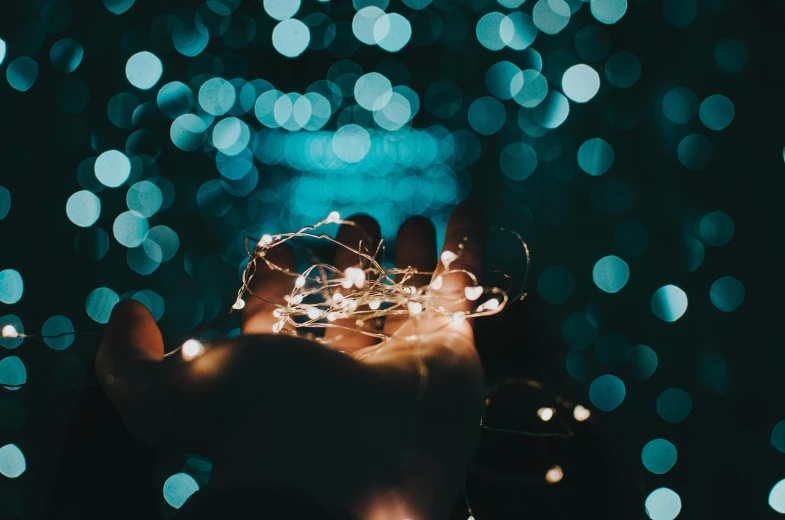 a person holding a string of lights in their hand, pexels contest winner, teal aesthetic, instagram post, bokeh”, sparkling cove