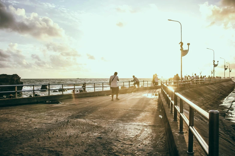 a man riding a skateboard down a sidewalk next to the ocean, by Niko Henrichon, unsplash contest winner, tel aviv street, light glare, people angling at the edge, near a jetty