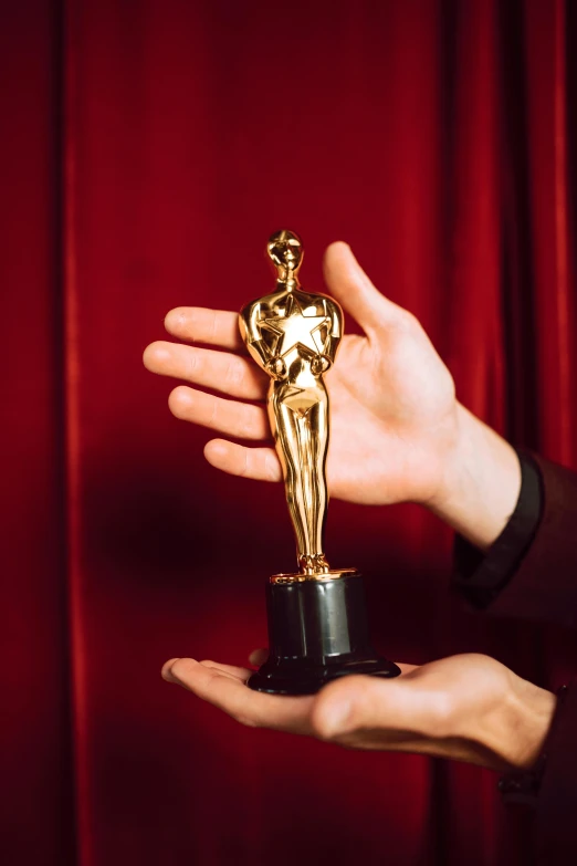 a person holding an oscar statue in their hand, pexels contest winner, art nouveau, 1980s photo, vhs, cinematic grade, red carpet photo